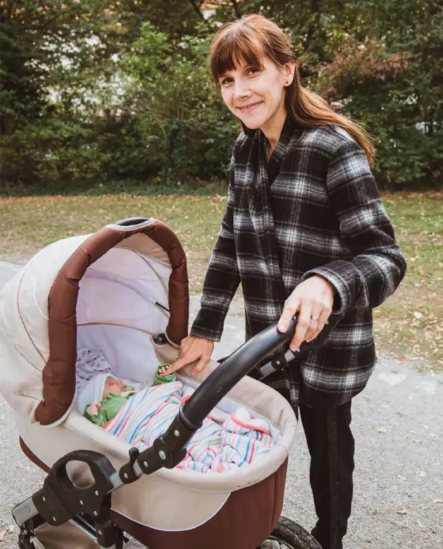 Baby sleep coach smiling next to a pram with a sleeping newborn during an outdoor walk – the Happy Baby Schlaf approach